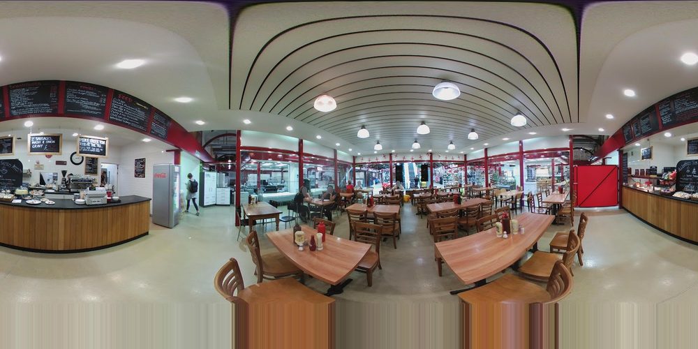 Wide view inside Bow Bells Cafe: the service counter, wooden tables and red-framed seating