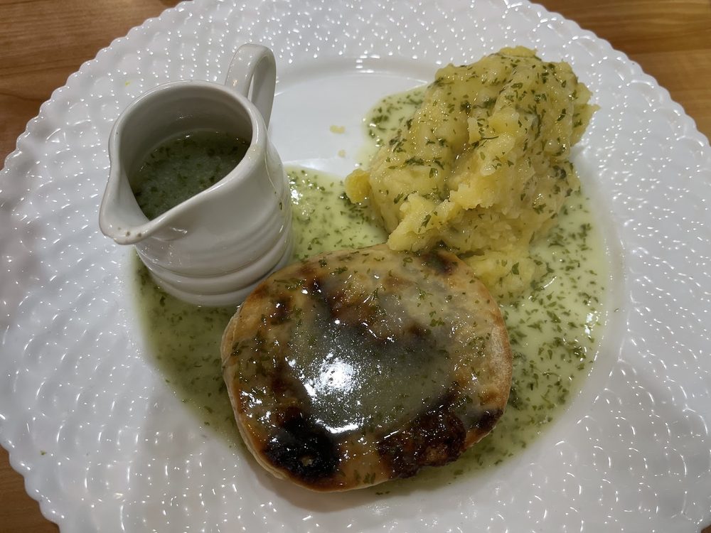Pie and mash with parsley liquor and a jug of extra liquor on a scalloped white plate