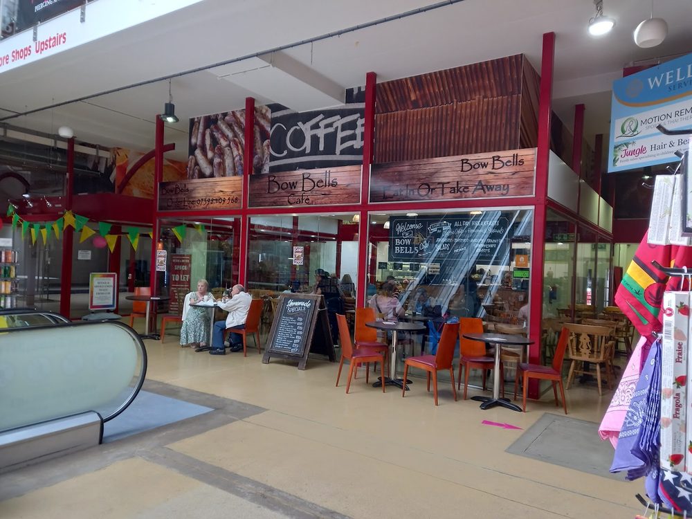The red shopfront of Bow Bells Cafe inside Romford's covered market arcade, with tables set out in front